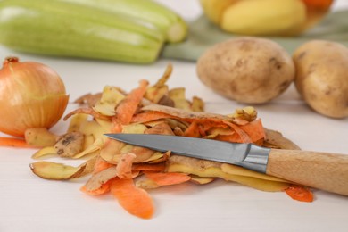 Peels of fresh vegetables and knife on white wooden table, closeup