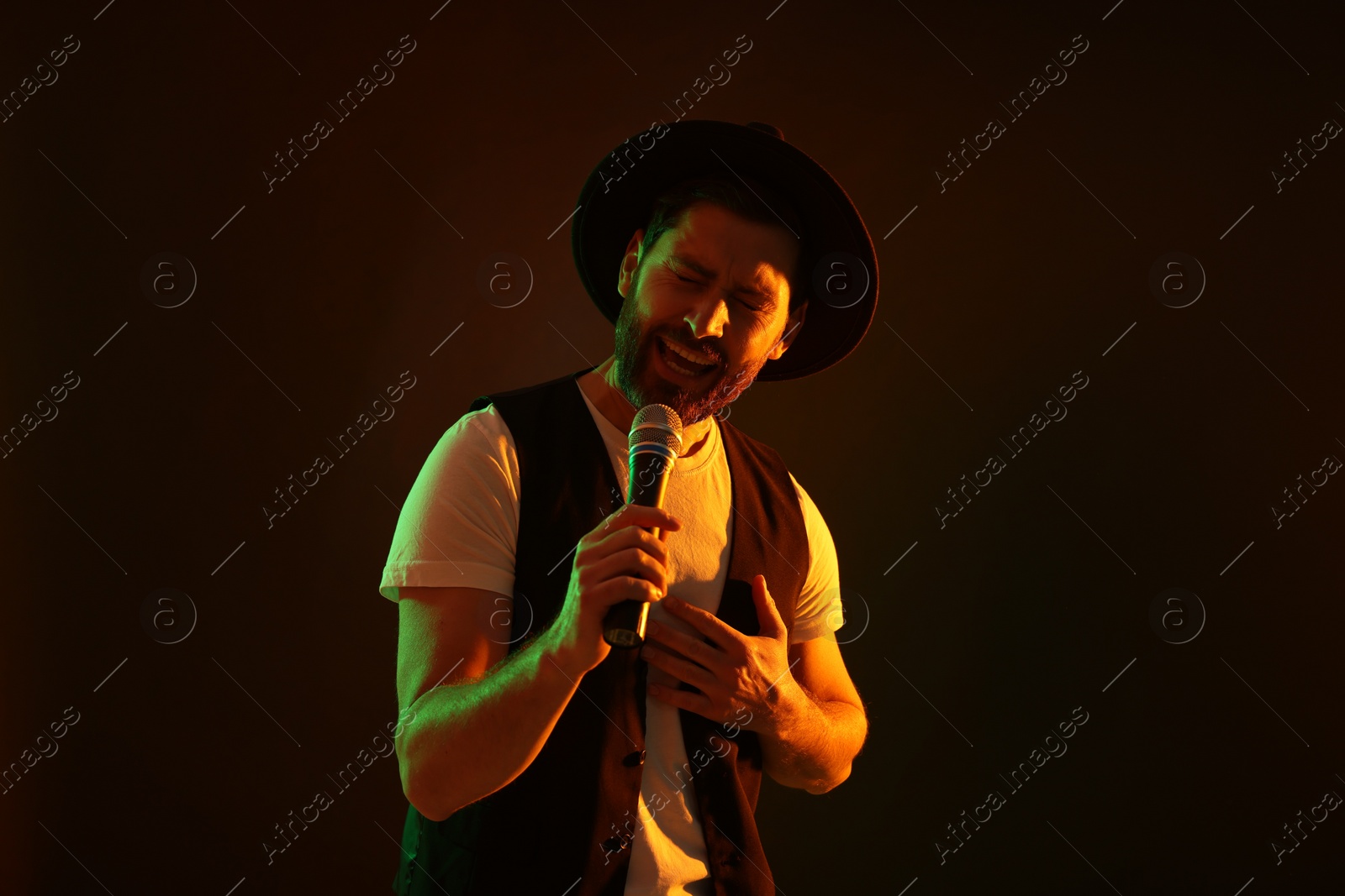 Photo of Handsome man with microphone singing in neon lights on dark background