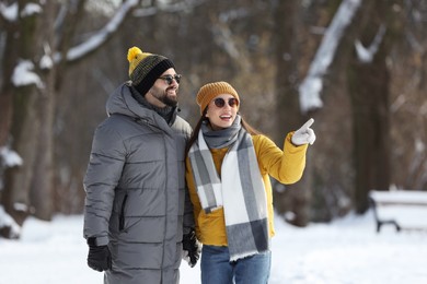 Happy young couple walking in snowy park on winter day
