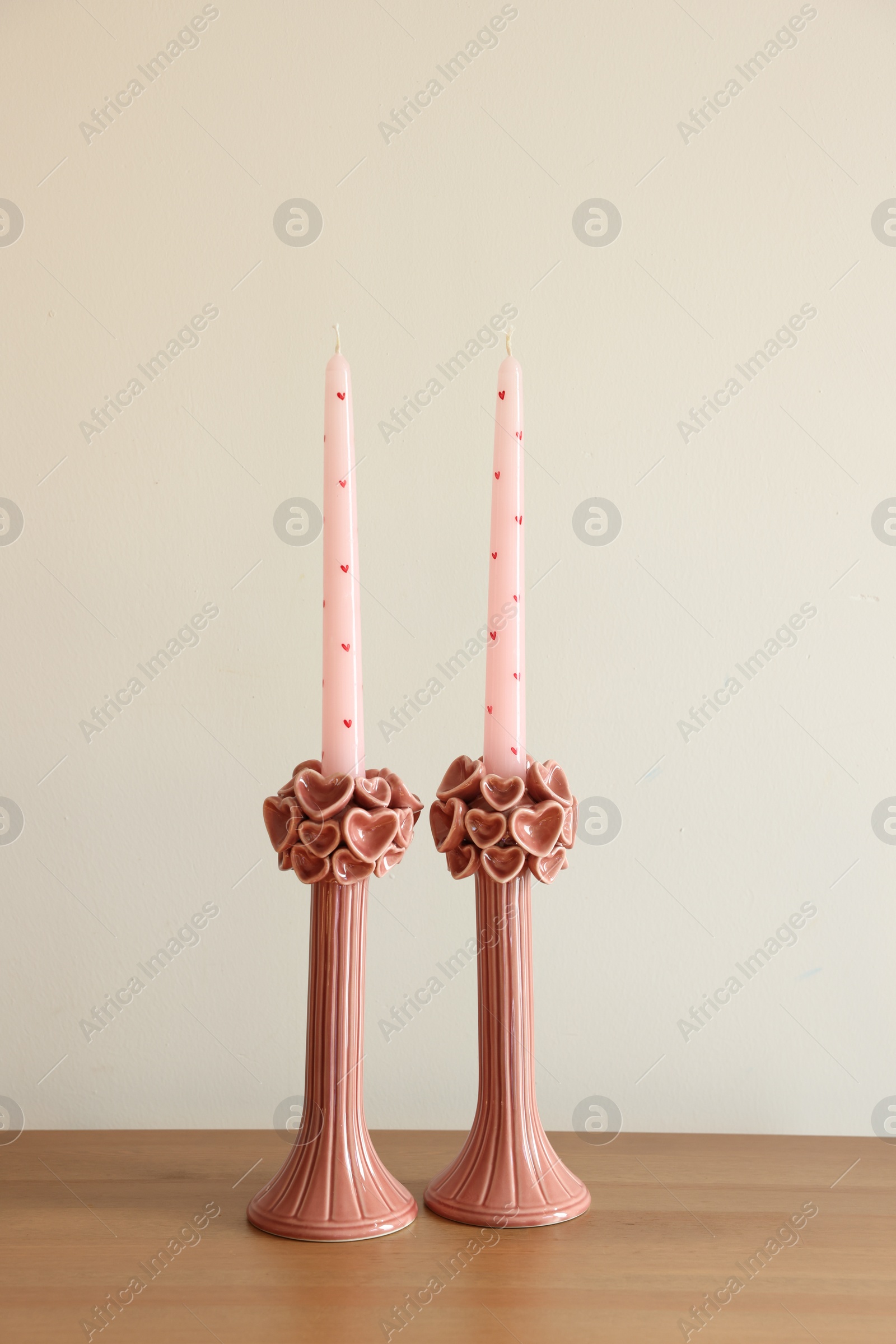 Photo of Beautiful pink wax candles on wooden table near white wall