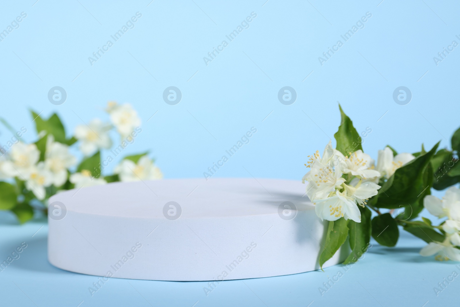 Photo of Presentation of product. White podium and beautiful jasmine flowers on light blue background, closeup. Space for text