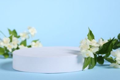 Photo of Presentation of product. White podium and beautiful jasmine flowers on light blue background, closeup. Space for text