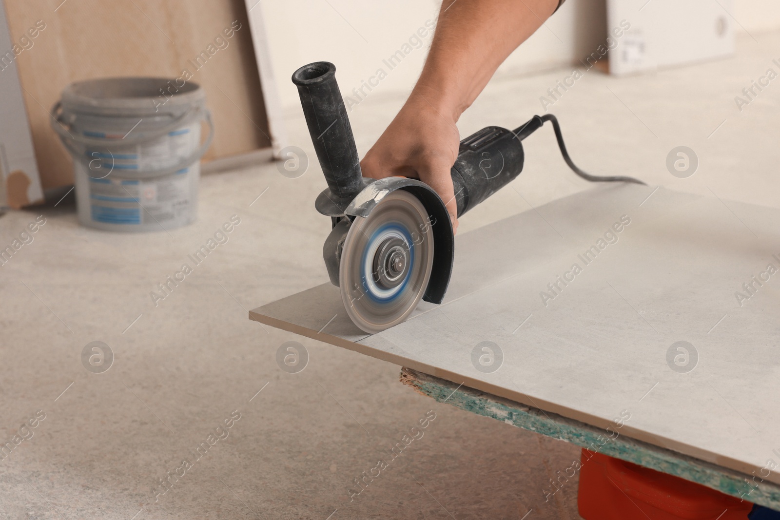 Photo of Worker using saw with circular diamond blade for tile cutting indoors, closeup