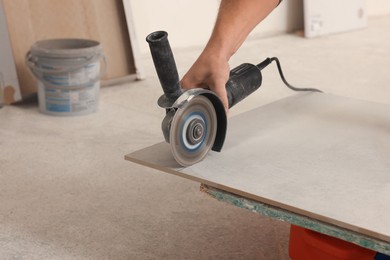 Photo of Worker using saw with circular diamond blade for tile cutting indoors, closeup