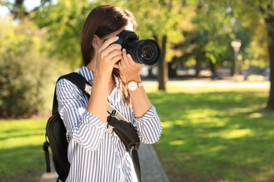 Young female photographer taking photo with professional camera in park. Space for text