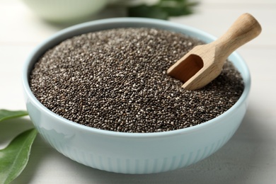 Bowl with chia seeds and wooden scoop on white table, closeup