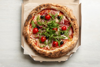 Photo of Tasty pizza with meat and arugula in cardboard box on white table, top view