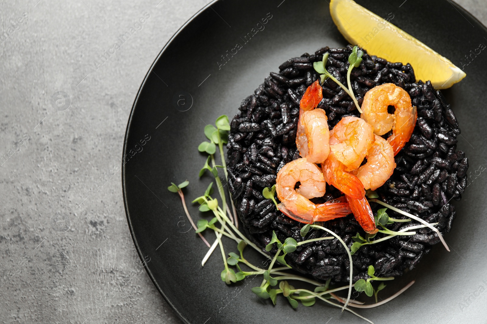 Photo of Delicious black risotto with shrimps and lemon on grey table, top view