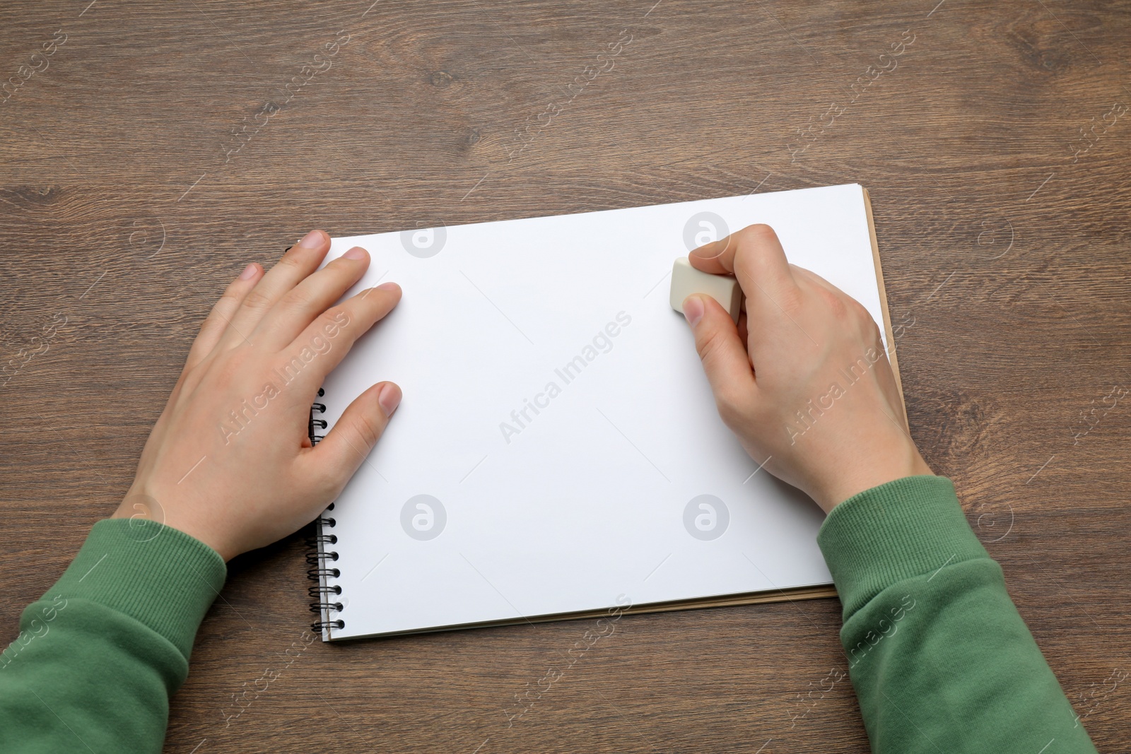 Photo of Man erasing something in notebook at wooden table, closeup