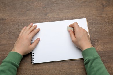 Photo of Man erasing something in notebook at wooden table, closeup