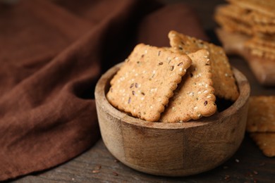 Photo of Cereal crackers with flax and sesame seeds in bowl on wooden table, closeup. Space for text