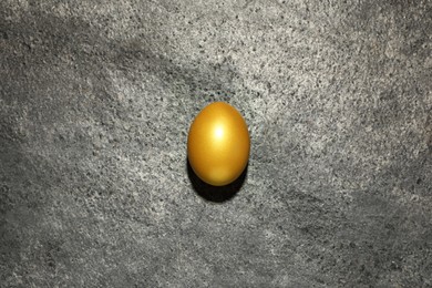 Photo of Shiny golden egg on grey table, top view