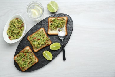 Delicious sandwiches with guacamole and lime wedges on white wooden table, flat lay. Space for text