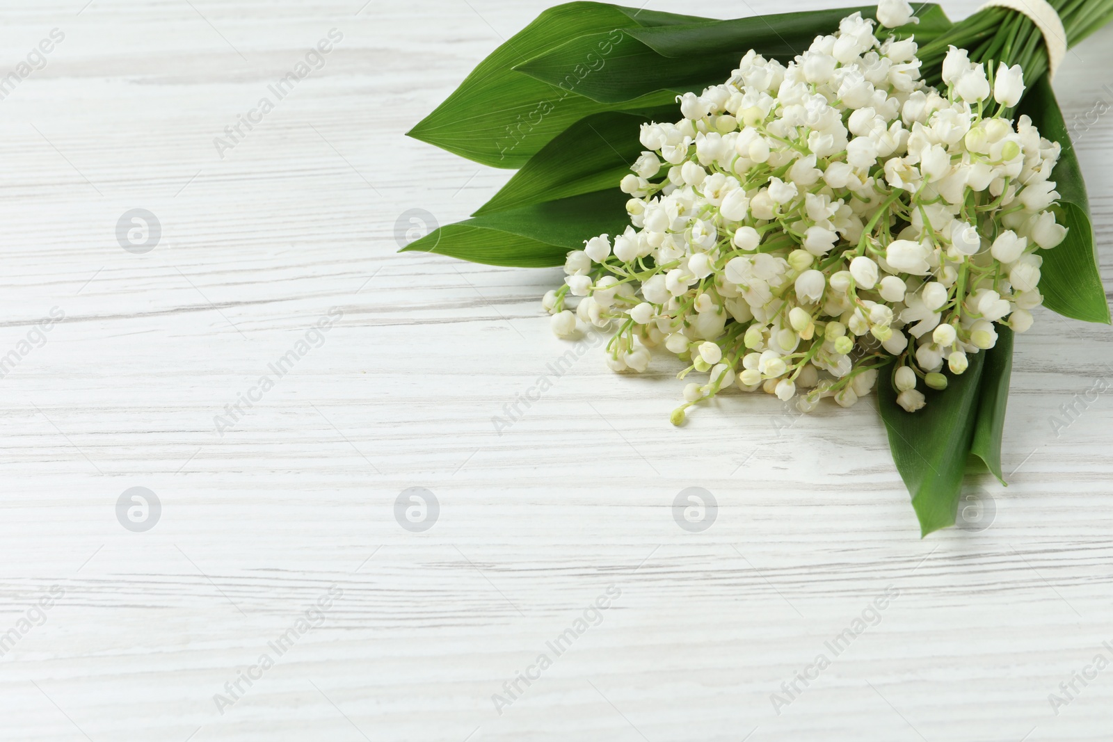 Photo of Beautiful lily of the valley bouquet on white wooden table, closeup. Space for text