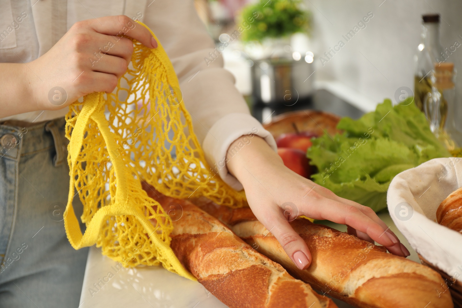 Photo of Woman taking baguettes out from string bag at countertop, closeup