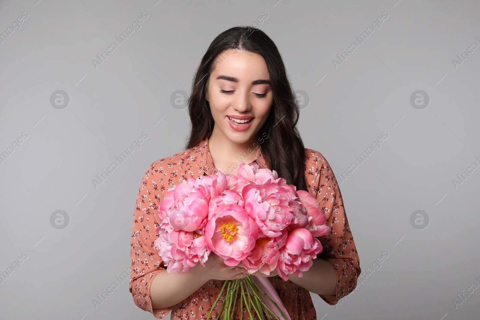 Photo of Beautiful young woman with bouquet of peonies on light grey background