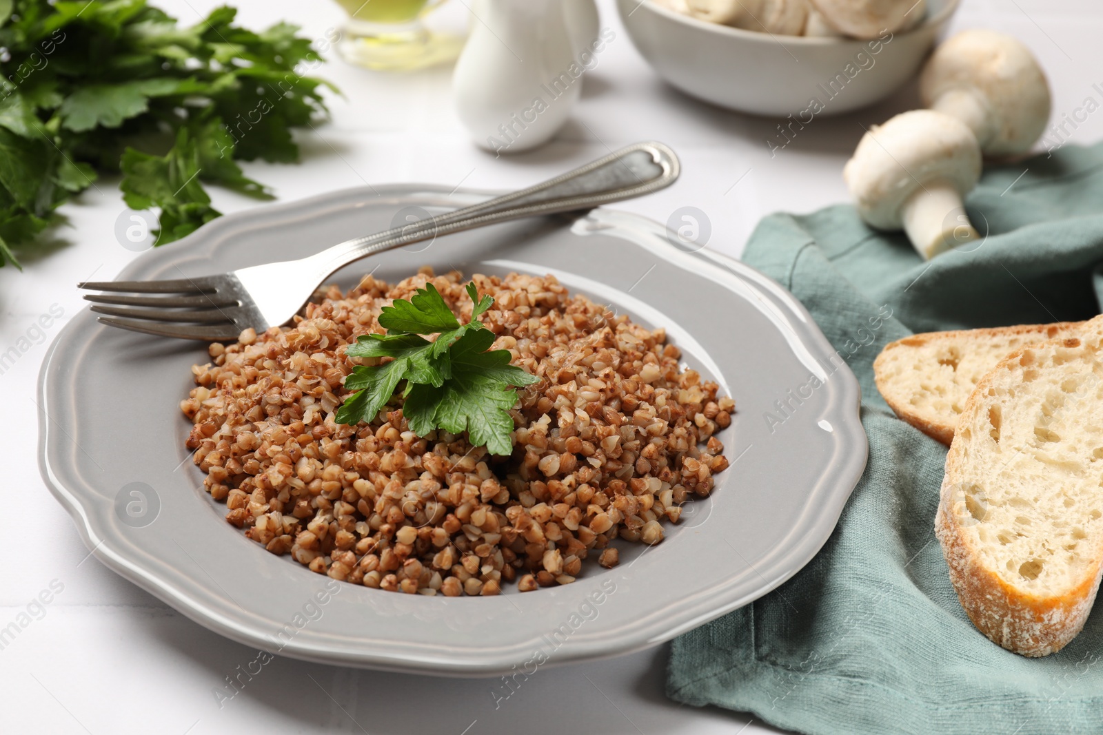 Photo of Tasty buckwheat with fresh parsley served on white tiled table