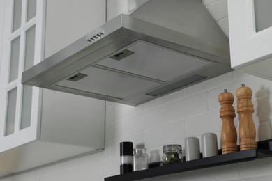 Photo of Modern range hood over shelf with spices in kitchen