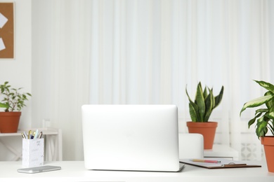Photo of Laptop on table and houseplants in office interior, space for text