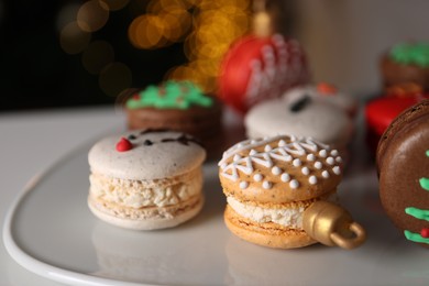 Photo of Beautifully decorated Christmas macarons on white table against blurred festive lights, closeup
