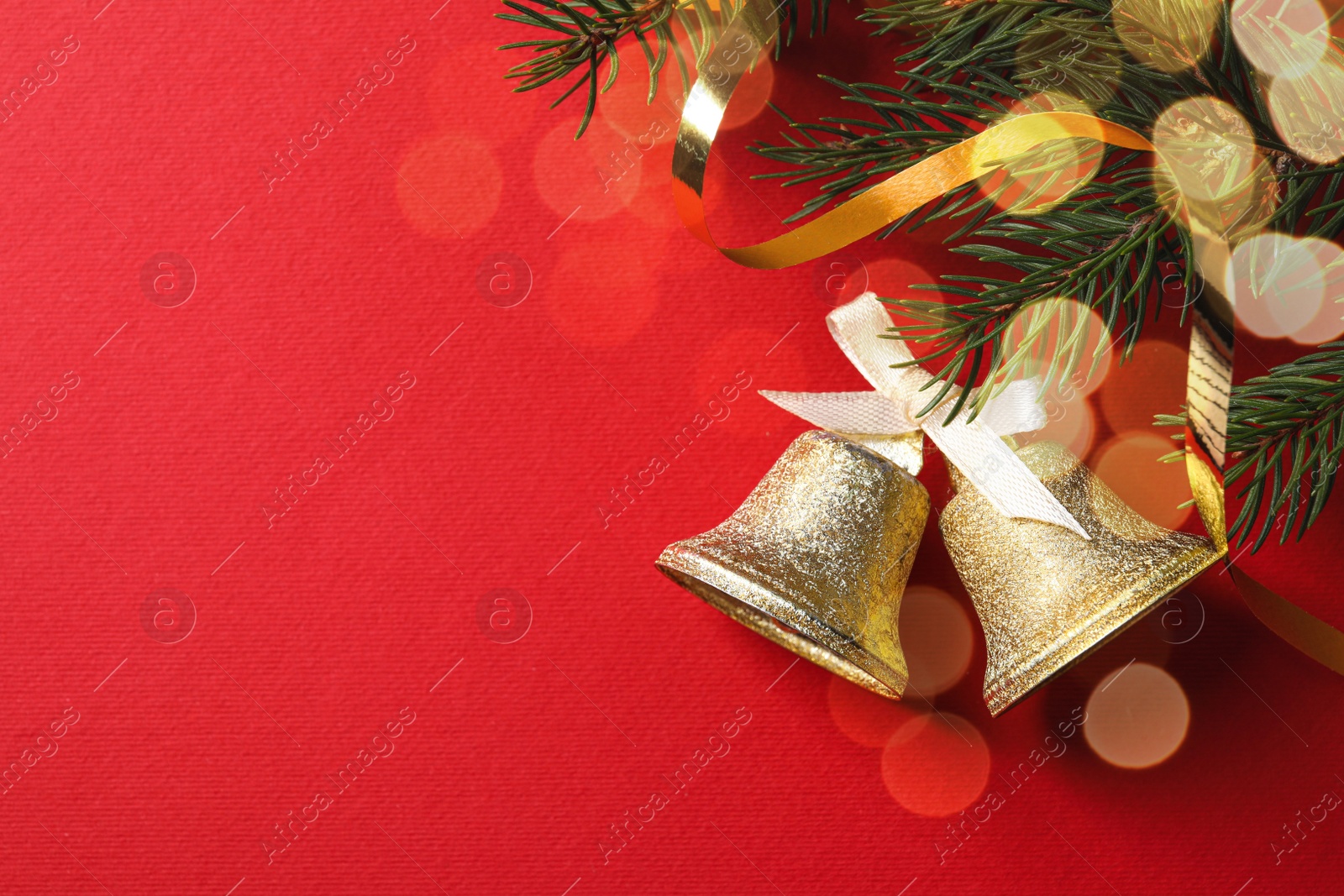 Photo of Christmas bells and fir tree branches on red background, flat lay. Space for text