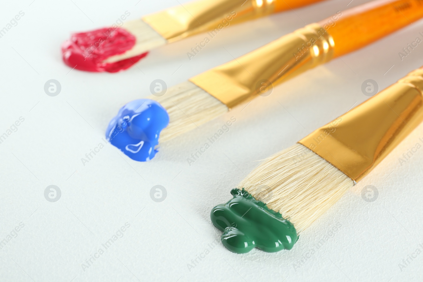 Photo of Brushes with bright paints on white background, closeup