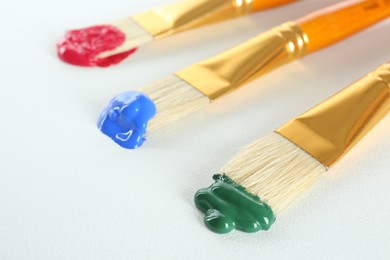 Brushes with bright paints on white background, closeup