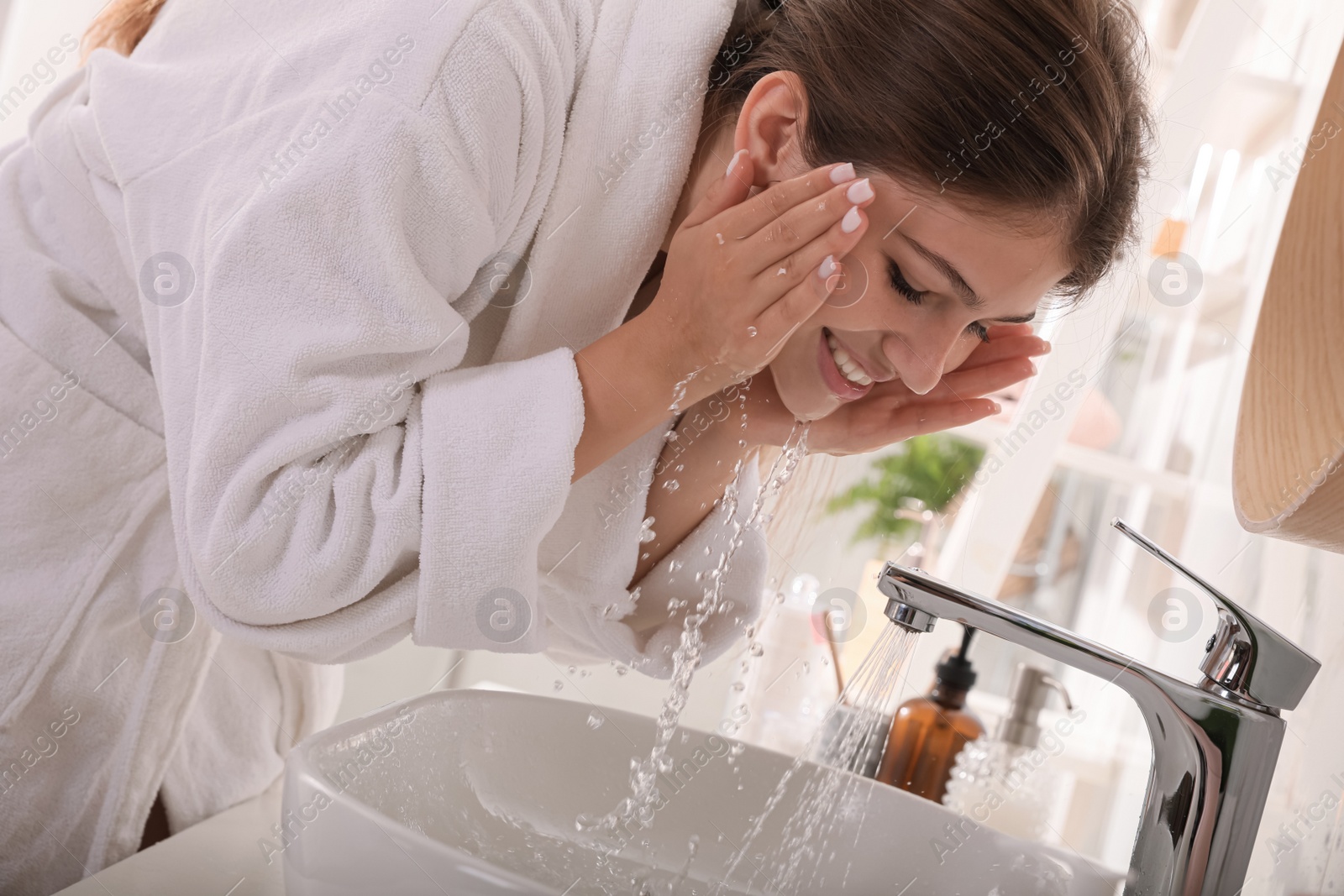 Photo of Beautiful teenage girl washing face with water in bathroom