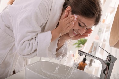 Beautiful teenage girl washing face with water in bathroom