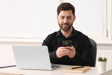 Photo of Smiling man using smartphone at table in office