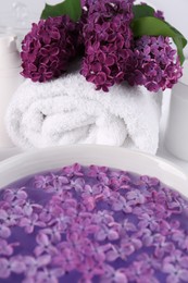 Photo of Lilac flowers with white towel and bowl of aromatic water on table, closeup