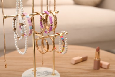 Photo of Holder with set of luxurious jewelry on wooden table in living room, closeup