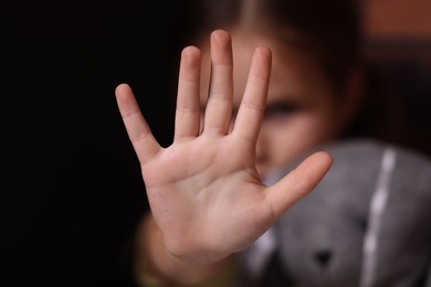 Photo of Child abuse. Little girl doing stop gesture on dark background, selective focus