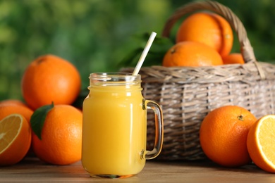 Photo of Delicious orange juice and fresh fruits on wooden table against blurred background