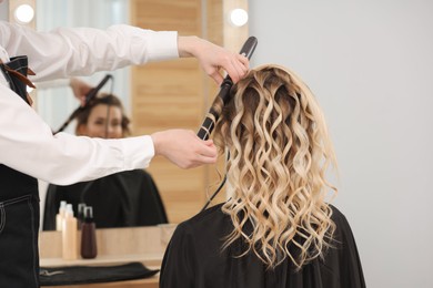 Hair styling. Hairdresser curling woman's hair in salon, closeup