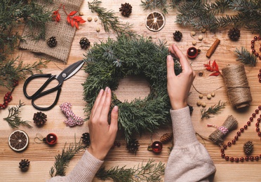 Photo of Florist making beautiful Christmas wreath at wooden table, top view