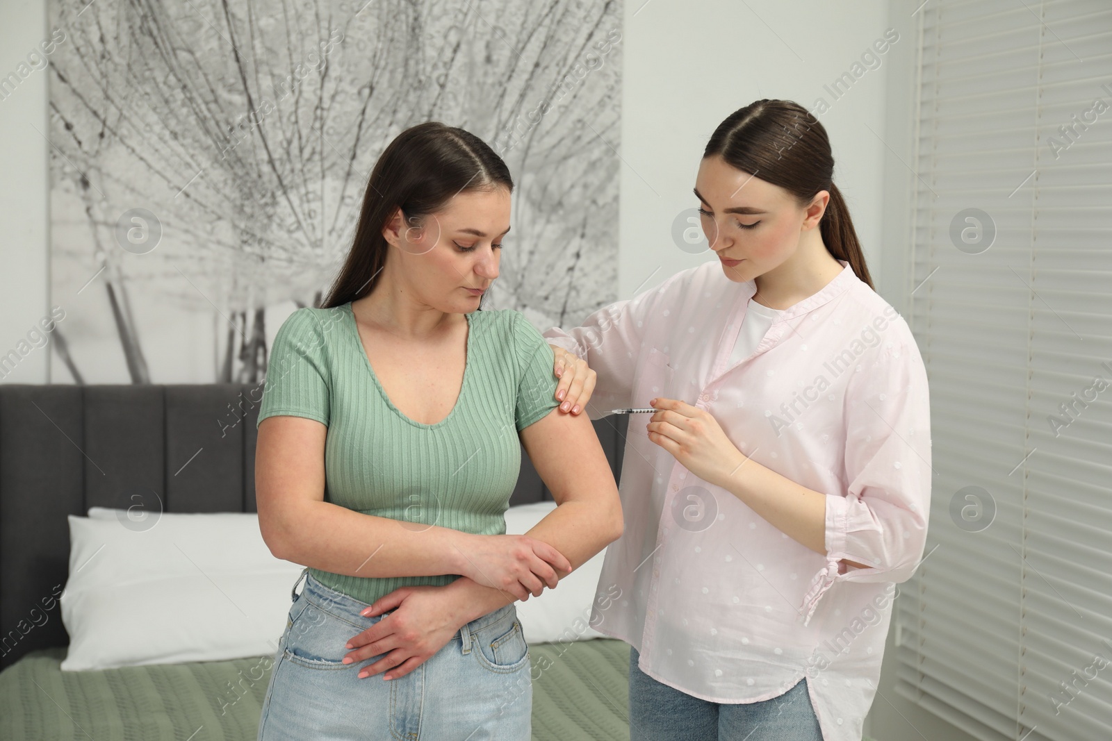 Photo of Woman giving insulin injection to her diabetic friend in bedroom