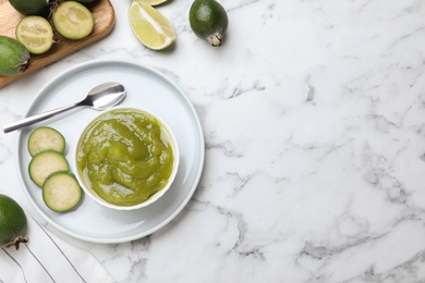 Photo of Feijoa jam and fresh fruits on white marble table, flat lay. Space for text