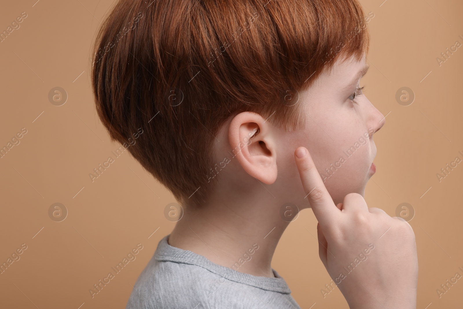 Photo of Little boy with hearing problem on pale brown background, closeup