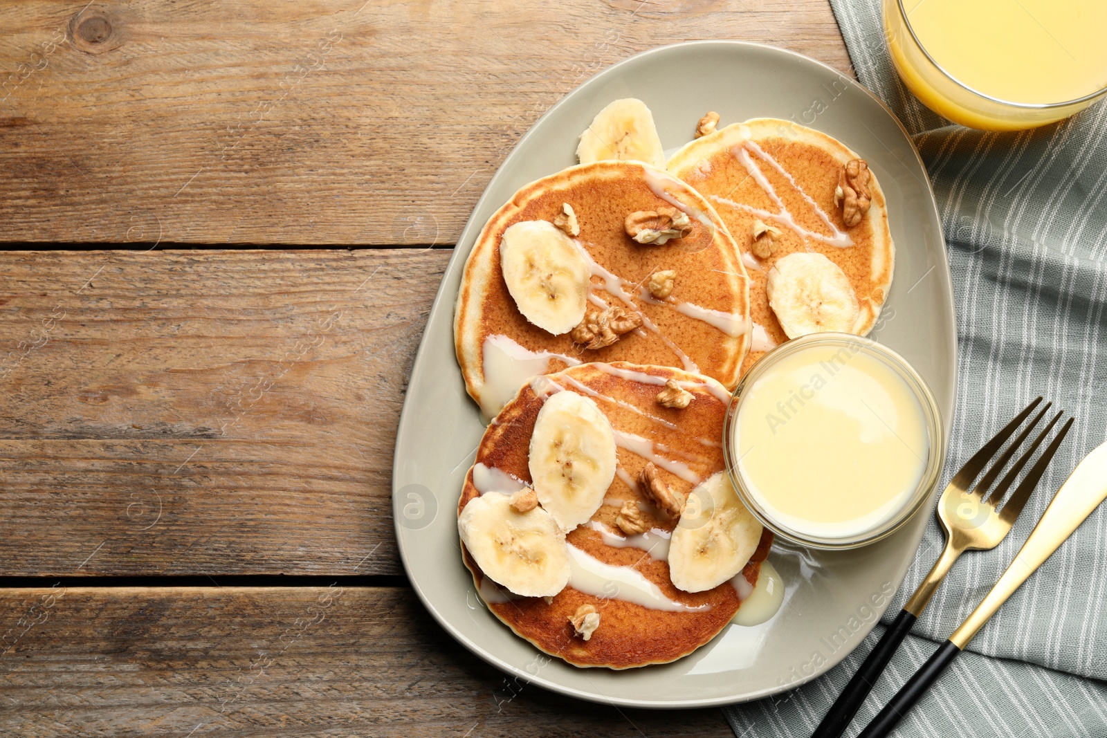 Photo of Tasty pancakes with sliced banana served on wooden table, flat lay. Space for text