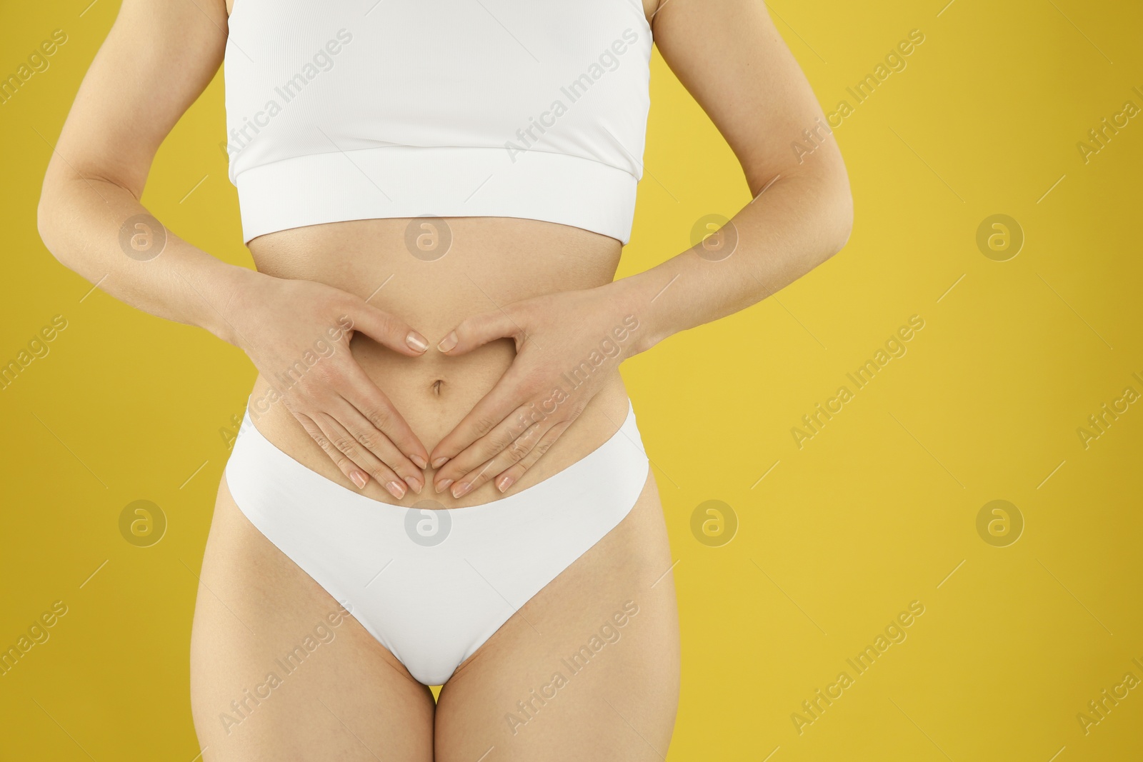 Photo of Gynecology. Woman in underwear making heart with her hands on yellow background, closeup. Space for text