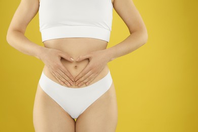 Photo of Gynecology. Woman in underwear making heart with her hands on yellow background, closeup. Space for text