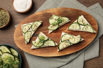 Photo of Tasty sandwiches with cream cheese, cucumber and microgreens on wooden table, flat lay