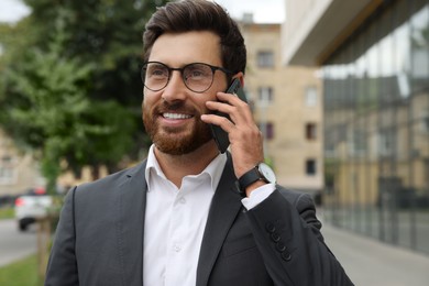 Handsome businessman talking on smartphone while walking outdoors