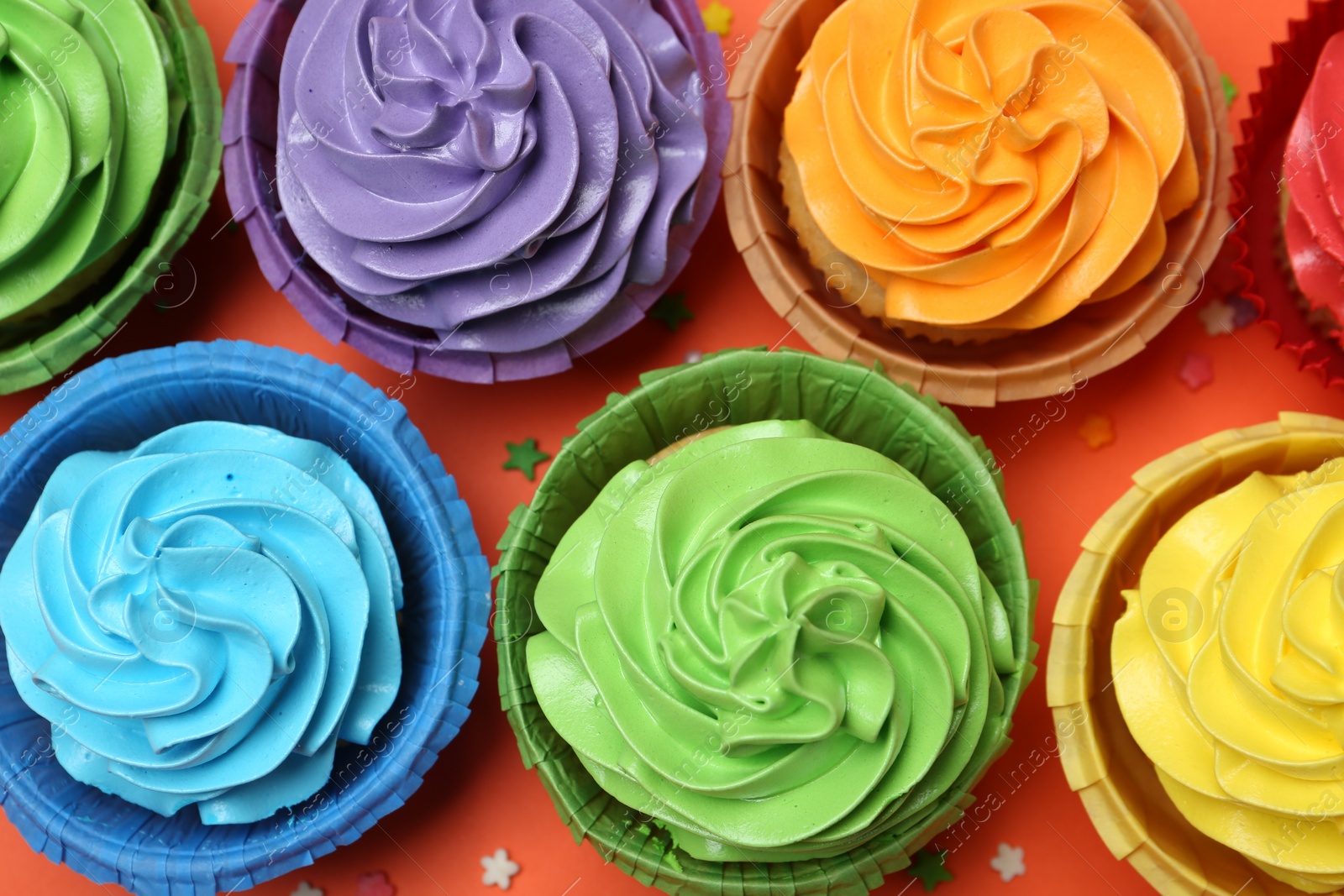 Photo of Delicious bright cupcakes and sprinkles on coral background, flat lay