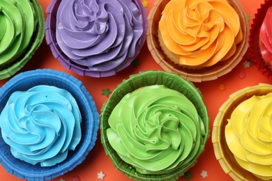 Photo of Delicious bright cupcakes and sprinkles on coral background, flat lay