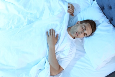 Young man sleeping in bed at night, top view