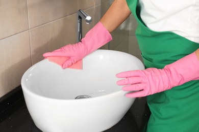 Woman in protective gloves cleaning bathroom sink with rag, closeup