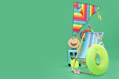 Photo of Deck chair, kite, suitcase and beach accessories on green background, space for text. Summer vacation