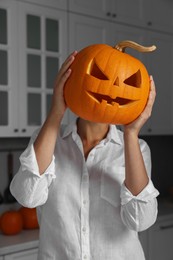Photo of Woman holding carved pumpkin for Halloween in kitchen